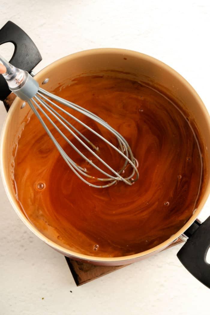 A pot of Panda Express Sweet and Sour Sauce, is being skillfully stirred with a whisk on the stove.