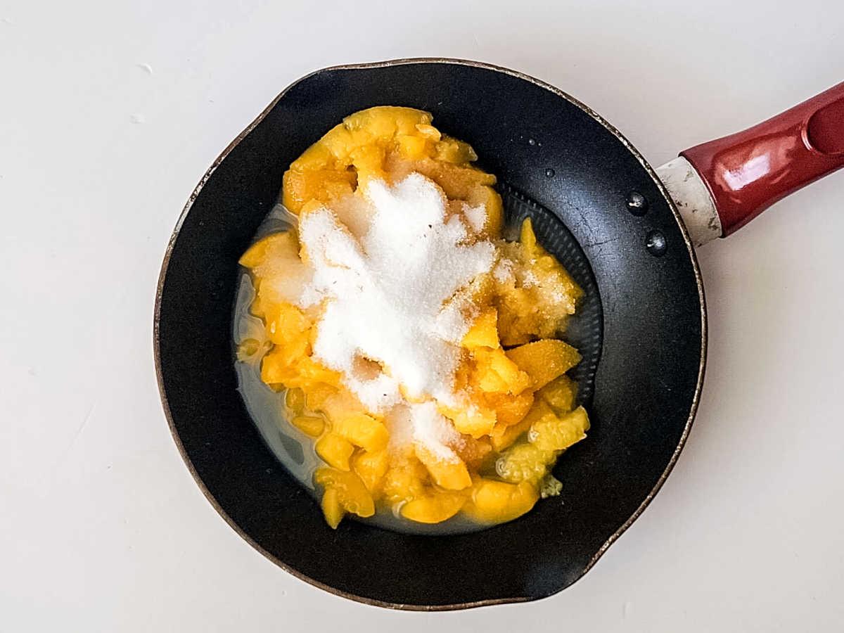 A frying pan with chopped peaches and sugar on a white surface, perfect for creating luscious peach bars with a tropical twist.