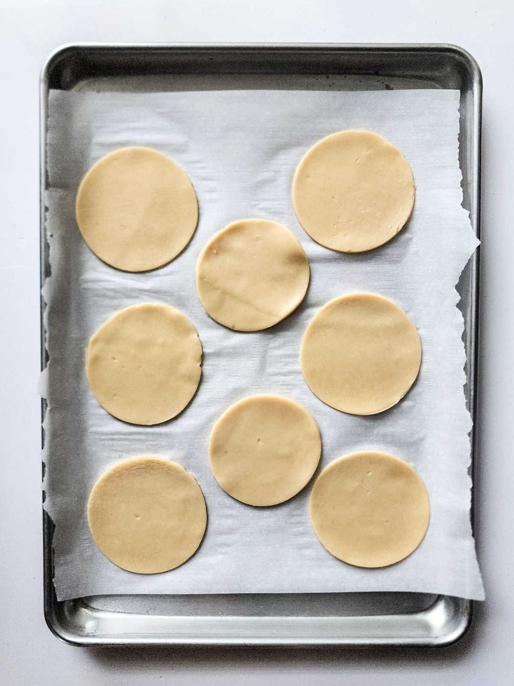 Eight round dough pieces, reminiscent of the gentle sweetness found in peach hand pies, rest poised on a parchment-lined baking sheet.