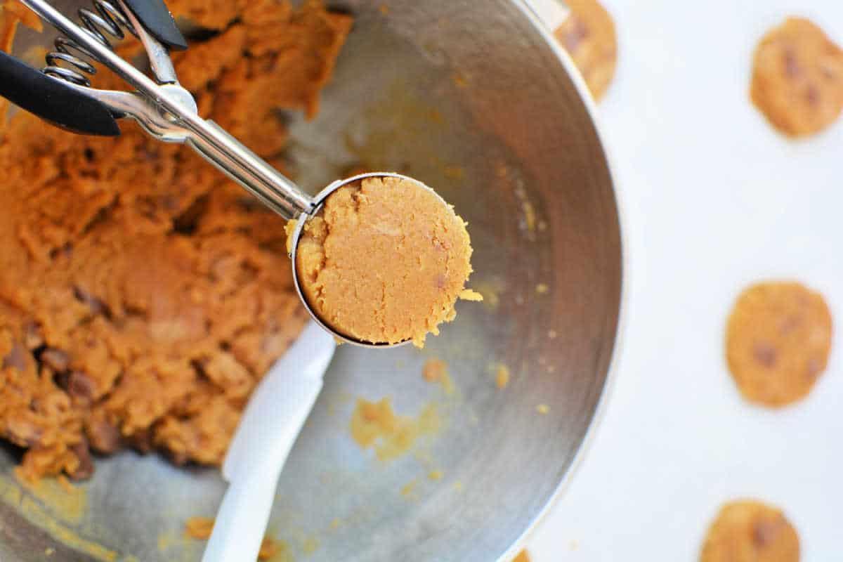 Cookie dough for peanut butter cookies in a metal scoop over a mixing bowl, ready to be placed on a baking sheet.