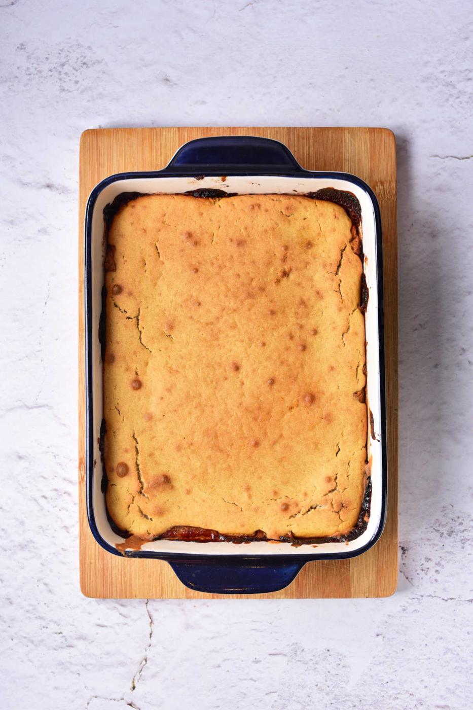 Baked cake in a rectangular blue and white dish on a wooden board, reminiscent of a Pear Upside Down Cake, placed on a textured white surface.
