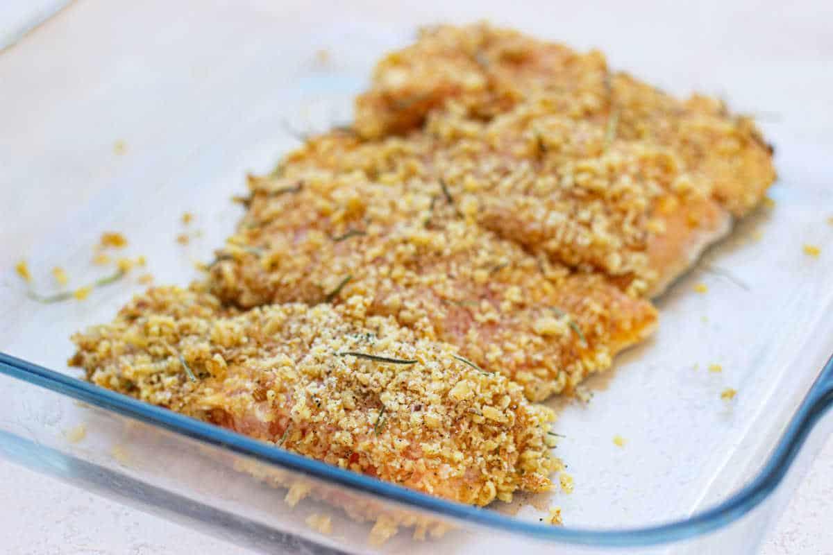Breaded fish fillets with herbs, reminiscent of pecan-crusted trout, sit in a glass baking dish, ready for cooking.