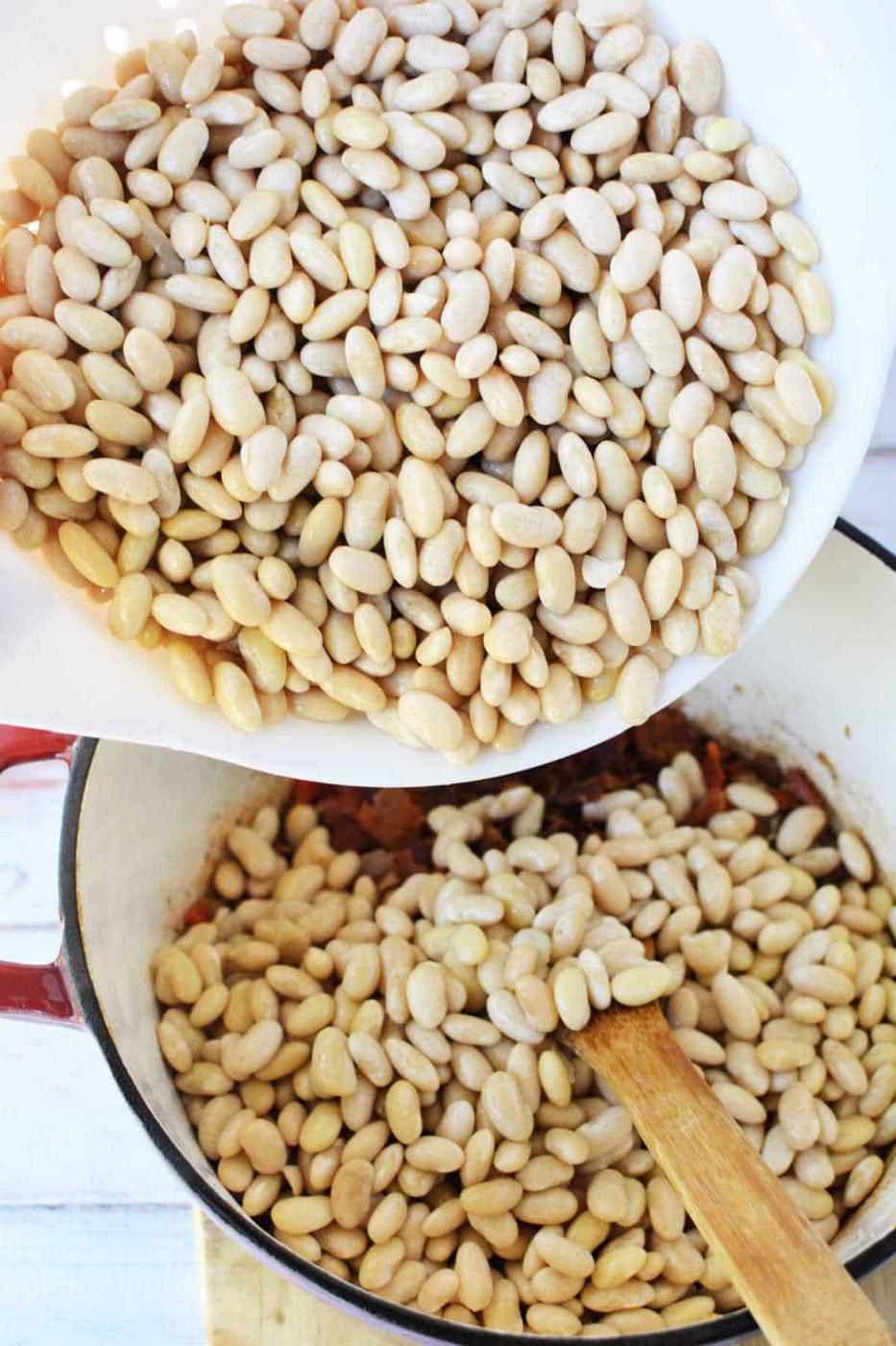 A bowl of Peruvian beans is being poured into a pot with a wooden spoon inside.