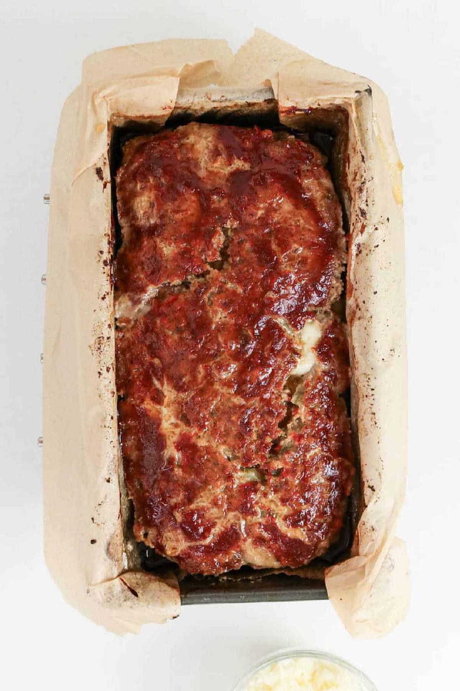 A Philly Cheesesteak Meatloaf baked in a parchment-lined loaf pan, topped with a shiny glaze for that irresistible finish.