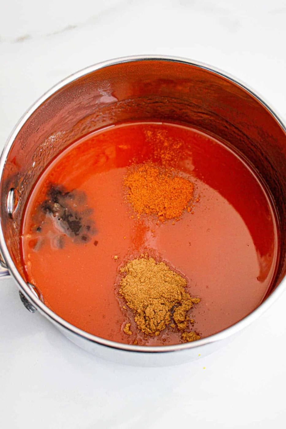 A steel pot brimming with a medley of spices evokes the vibrant kick of Popeyes Sweet Heat Sauce, all resting on a pristine white surface.