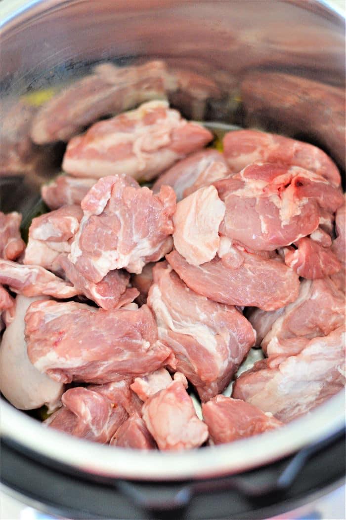 Raw chunks of pork meat piled inside a metal pot, ready to be transformed into savory pork adobo in the Instant Pot.
