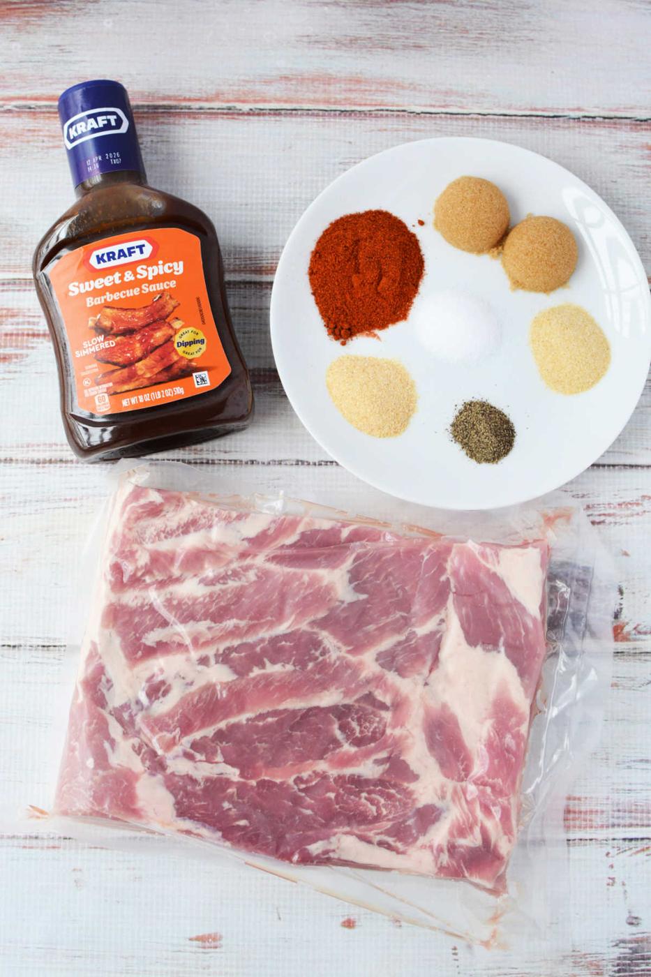 A slab of raw pork ribs, barbecue sauce, and a plate of six different spices await your next recipe on a white wooden surface—perfect for crafting smoky burnt ends or experimenting with pork belly delights.
