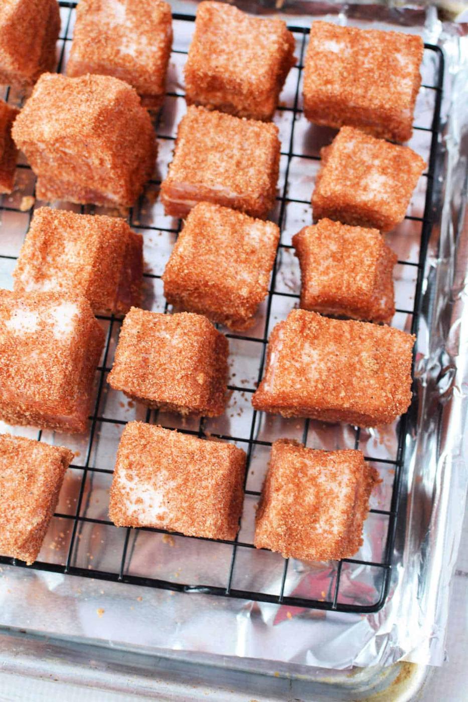 Squares of pork belly coated in a reddish-brown seasoning rest on a wire rack over a foil-lined tray, perfect for a savory burnt ends recipe.