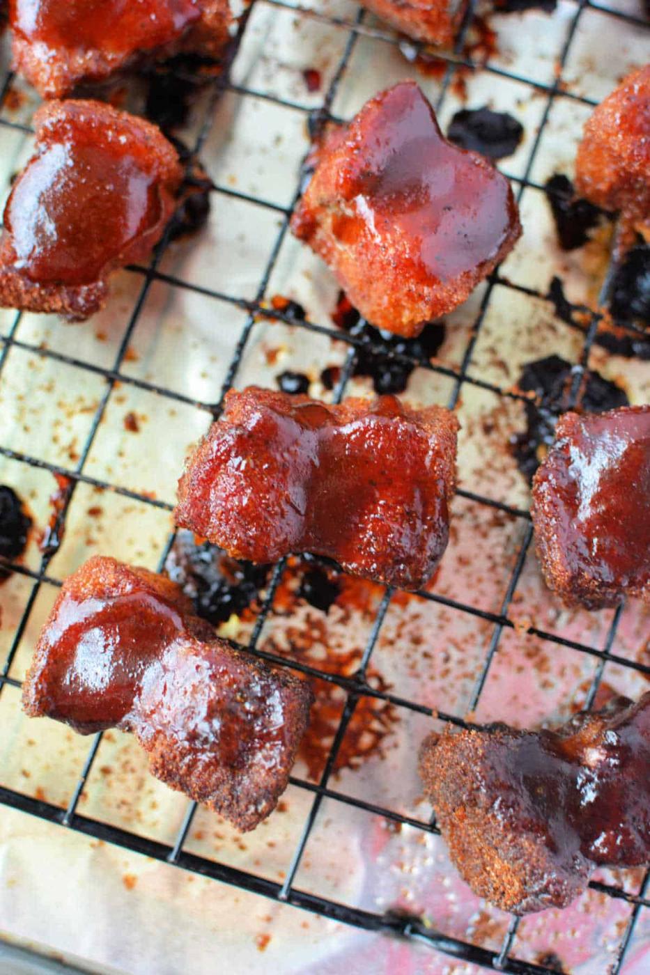 Crispy glazed pork belly burnt ends cooling on a wire rack over a foil-lined baking sheet—a mouthwatering recipe in the making.