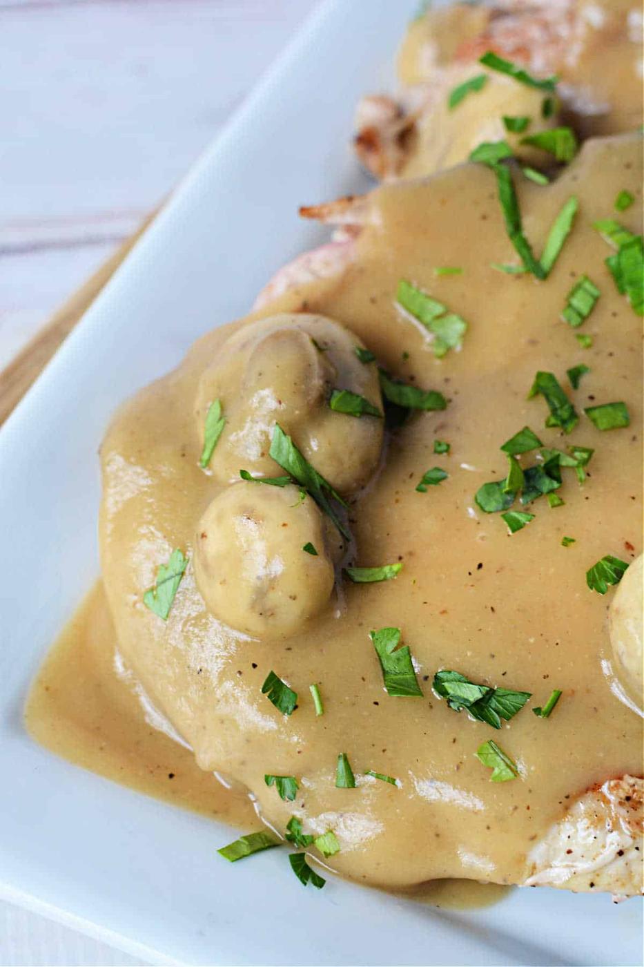 Plate of pork with creamy mushroom sauce, reminiscent of pork chops with mushroom gravy, garnished with chopped parsley.