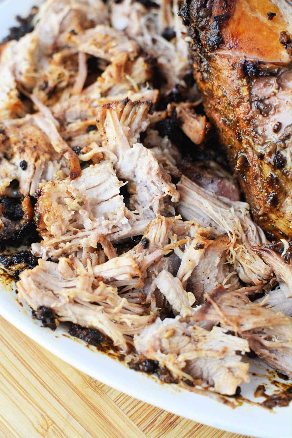 Shredded, seasoned pork roast on a white plate atop a wooden surface—perfect for showing off your favorite oven pork roast recipe.