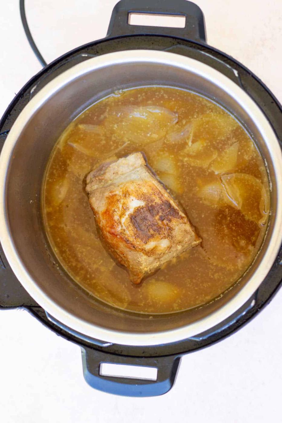 A savory pork roast cooks to perfection in an Instant Pot, surrounded by chopped onions and simmering broth.