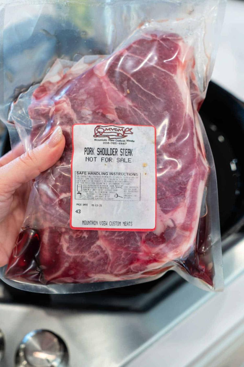 A hand holds a vacuum-sealed package of Pork Shoulder Steak labeled Not For Sale.