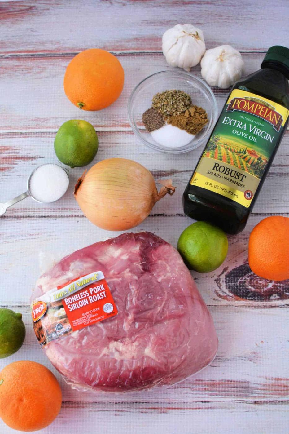 A delectable roast recipe awaits with ingredients like succulent pork, aromatic onions, zesty citrus fruits, spices, garlic, and olive oil elegantly arranged on a wooden surface.