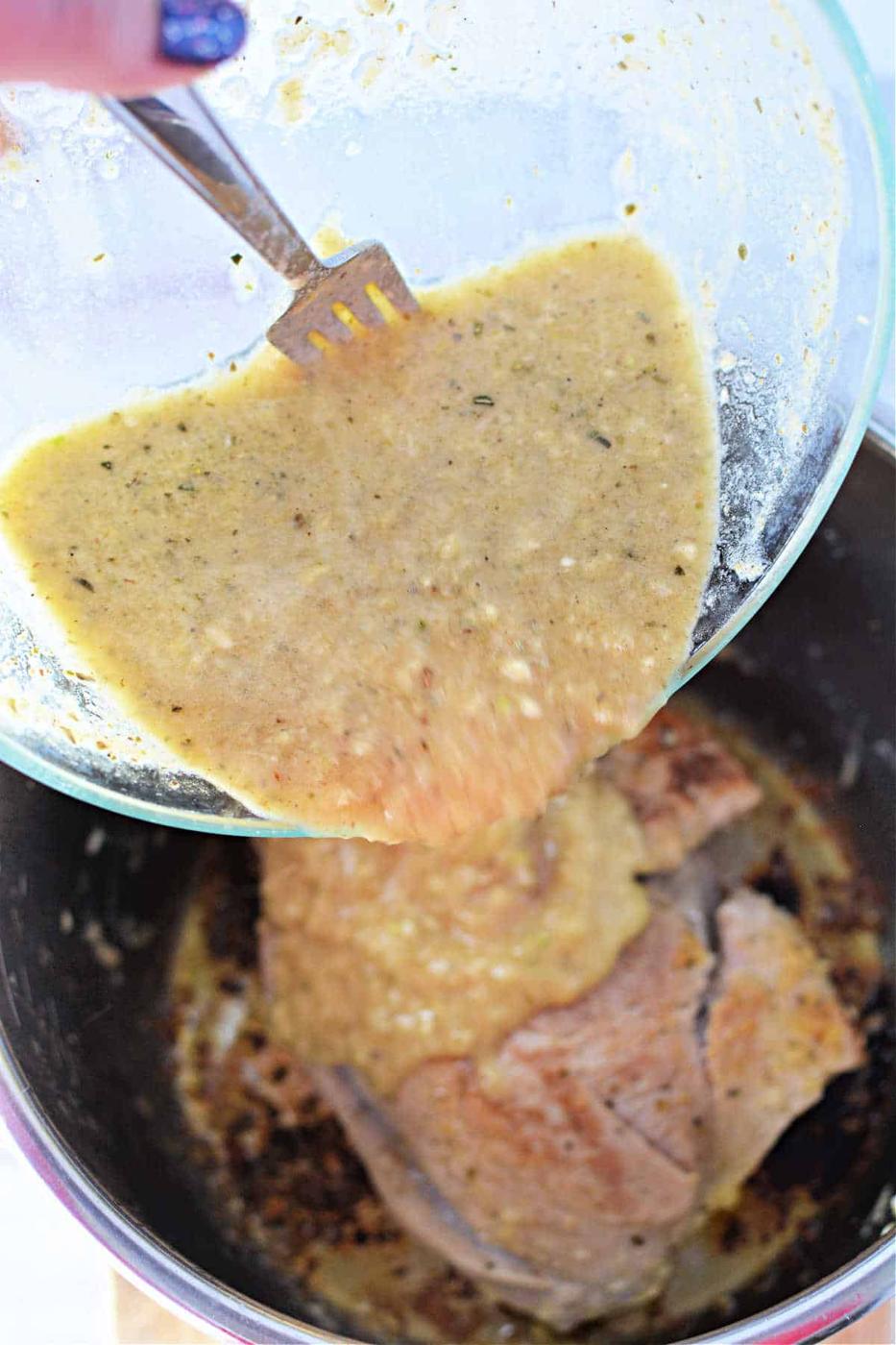 Pouring yellow marinade over pork in a pot, using a fork to scrape from a glass bowl.