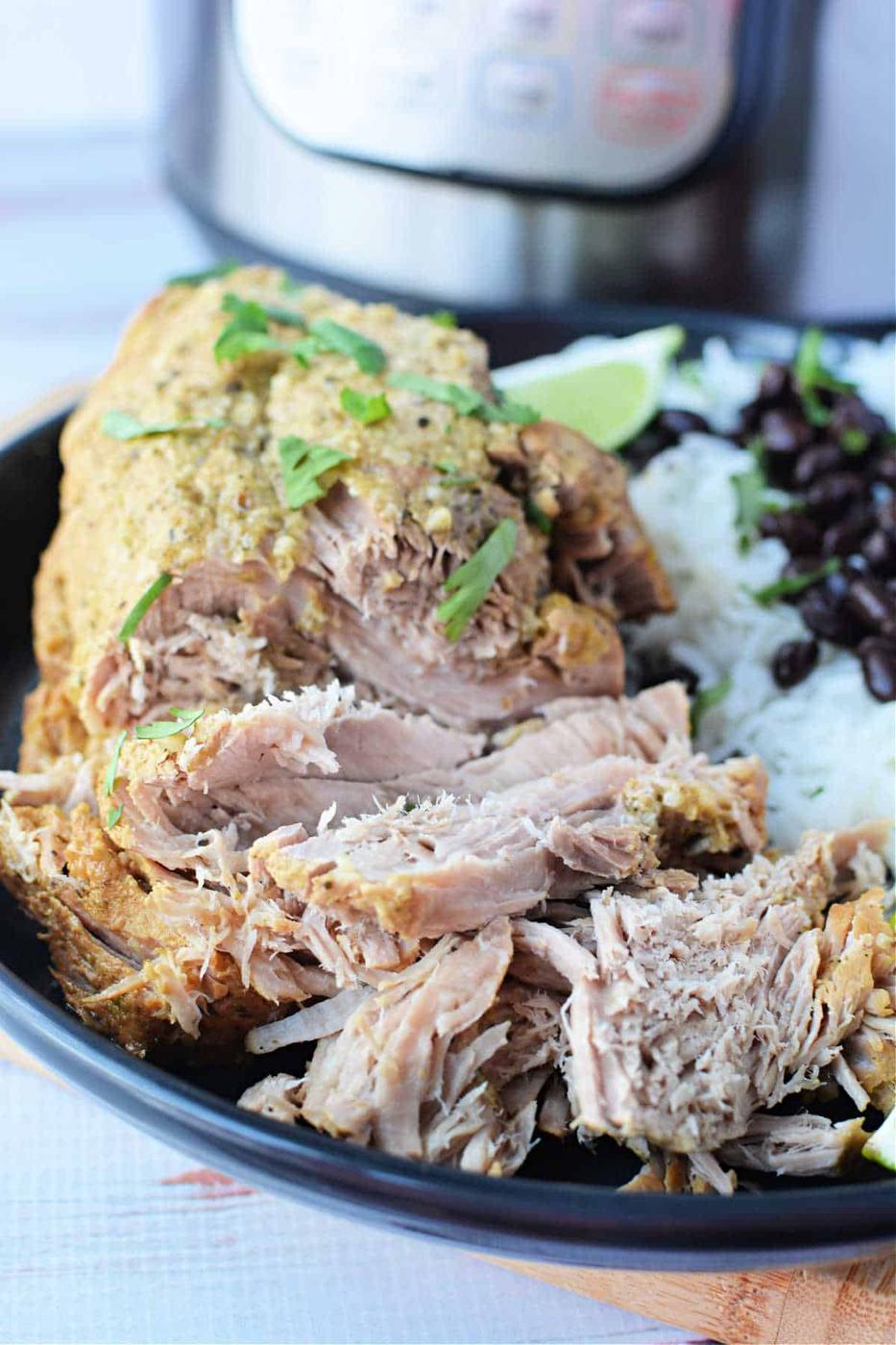 A delightful recipe featuring shredded pork sirloin roast in green sauce, elegantly served with rice, black beans, and lime wedges on a sleek black plate.