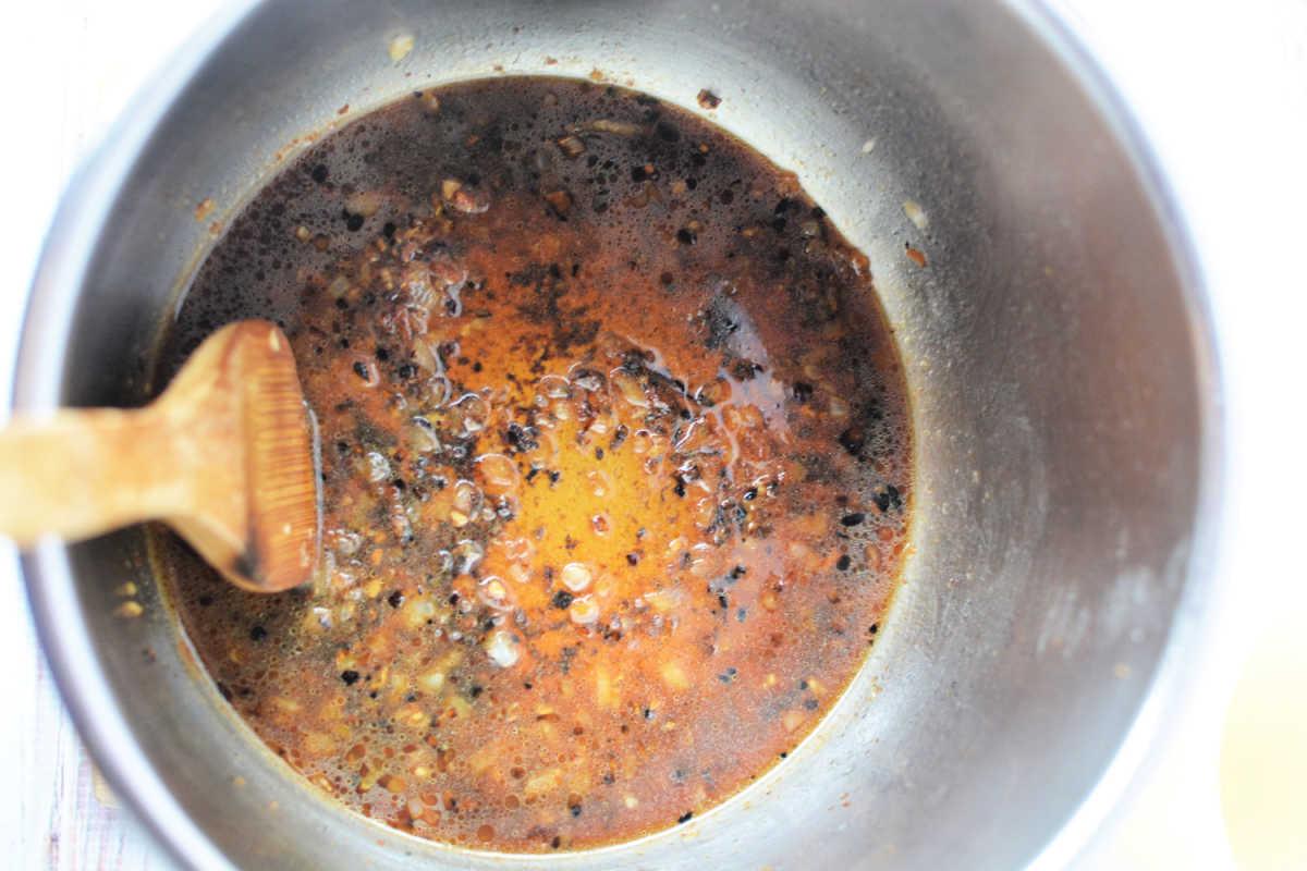 A pressure cooker pot with a wooden spoon, filled with a simmering dark brown, oily sauce with seasonings—perfect for enhancing your favorite Pork Steak Recipe.
