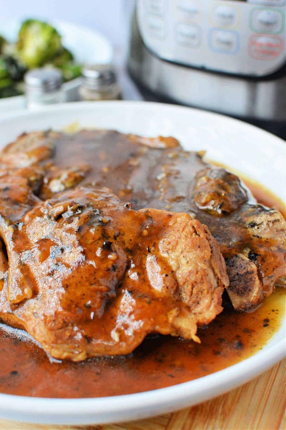Plate of tender pork steaks covered in brown gravy, featuring a delicious Pork Steak Recipe. An Instant Pot and broccoli are visible in the background, hinting at a wholesome homemade Pork Steak meal.