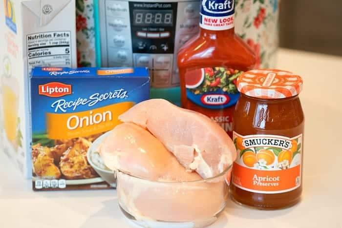 Raw chicken breasts in a bowl with onion soup mix, French dressing, apricot preserves, and an Instant Pot behind—perfect for making pressure cooker apricot chicken.