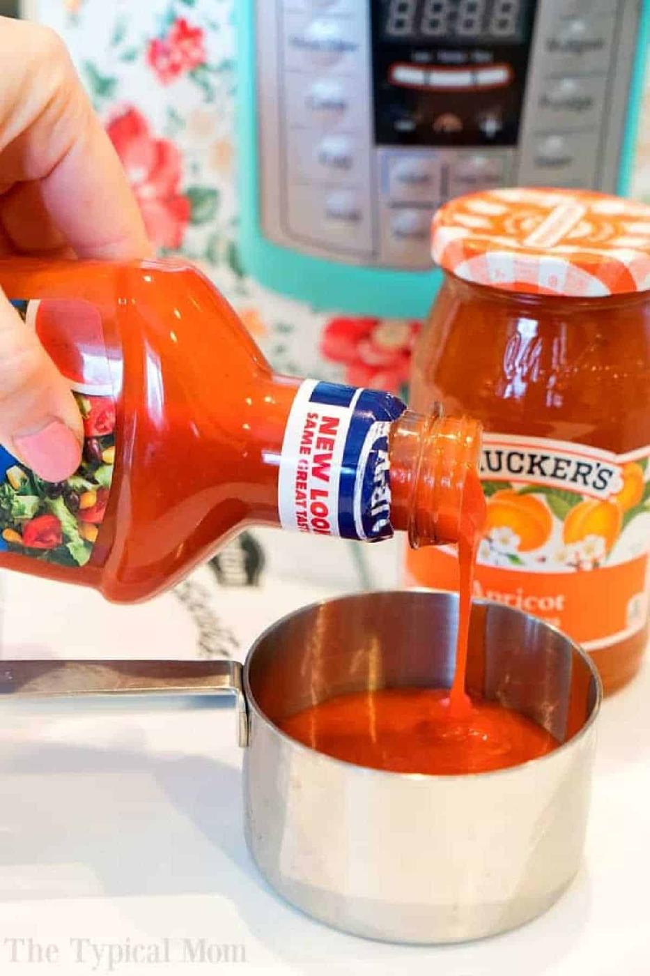 Hand pouring catalina dressing into a measuring cup, with a jar of apricot preserves in the background—perfect ingredients for pressure cooker apricot chicken.