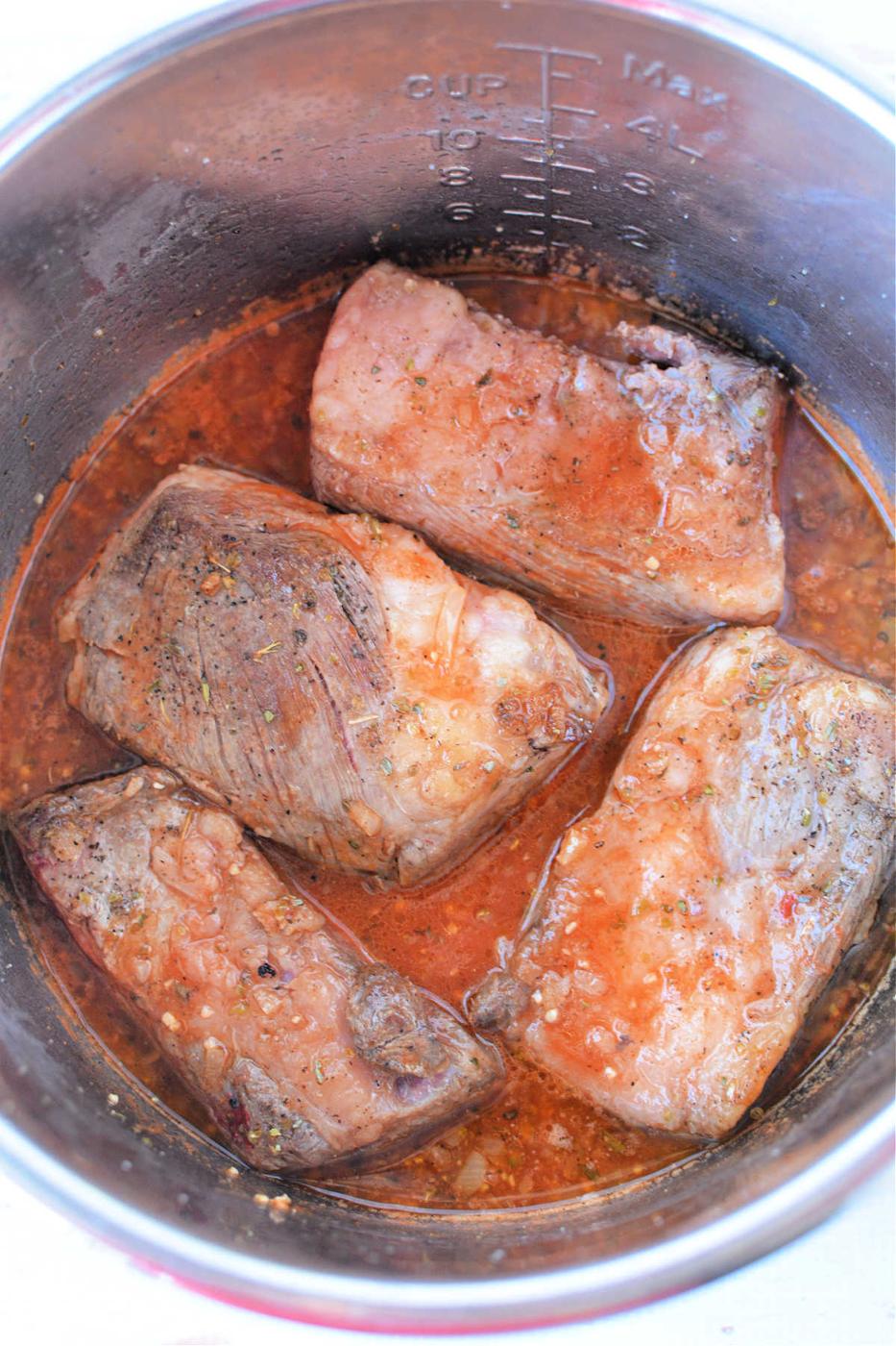 Tender beef ribs simmer in a rich red sauce inside a stainless steel pot, infusing each bite with mouthwatering flavor.