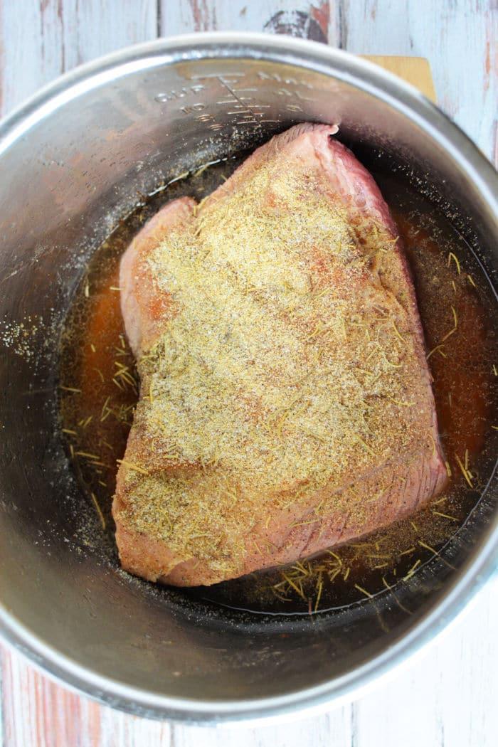 Raw brisket with seasoning sits in a metal pot, ready for transformation into a tender delight, perfect for your pressure cooker brisket recipe.