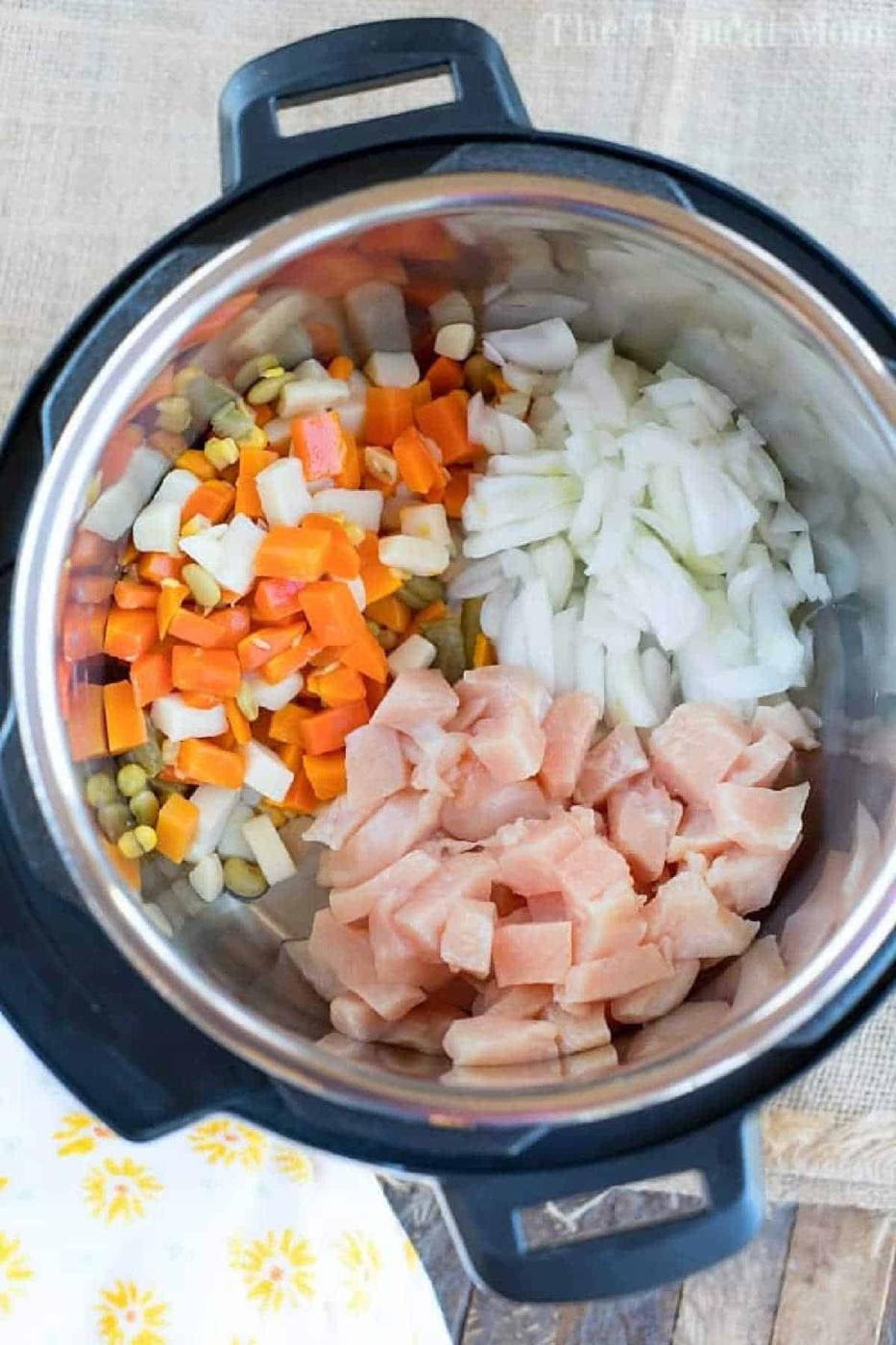 Chopped chicken, onions, and mixed vegetables in an Instant Pot, ready to be cooked into a hearty chicken pot pie soup.