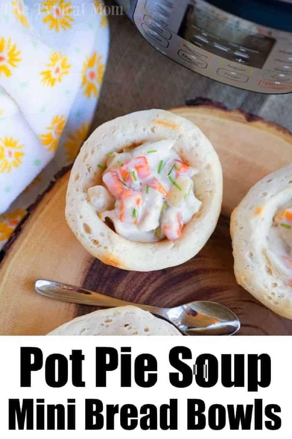 Mini bread bowl filled with creamy chicken pot pie soup, topped with chives, on a wooden board near a spoon.