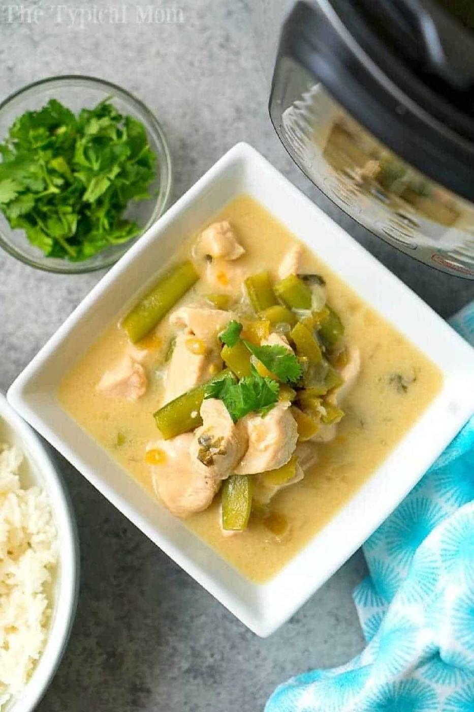 Square bowl of creamy coconut chicken curry with green beans, next to rice, cilantro, and an Instant Pot.