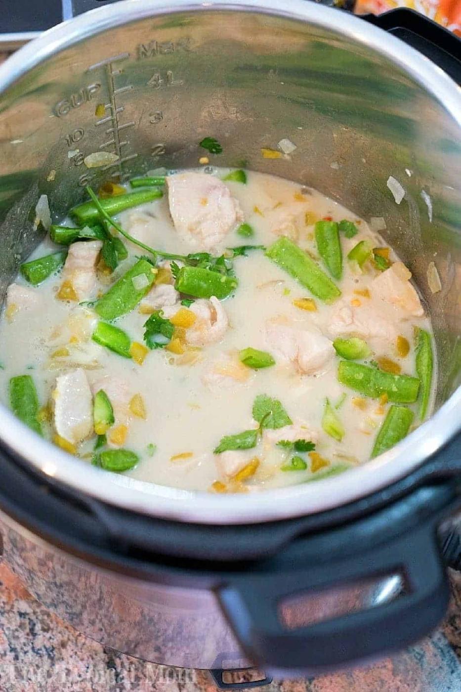 Coconut chicken, green beans, and herbs simmer in a creamy sauce inside an open Instant Pot on a kitchen counter.