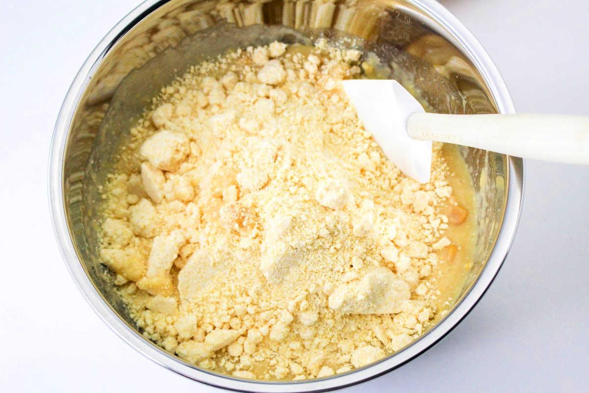 A mixing bowl with crumbly dough for pressure cooker cornbread and a white spatula rests on a white surface.