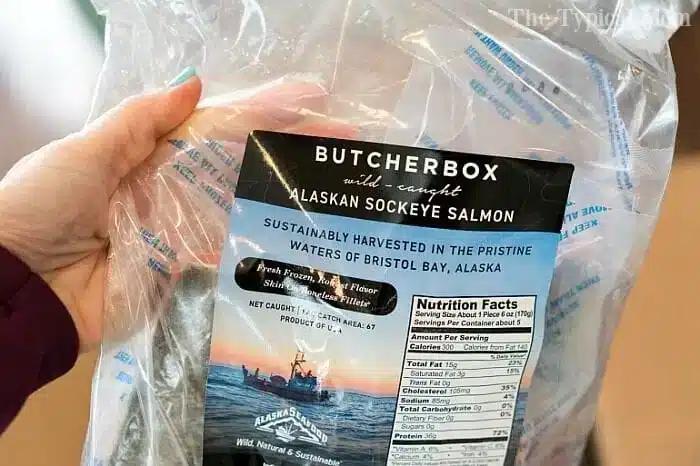 A hand holds a package of ButcherBox wild-caught Alaskan sockeye salmon, perfect for pressure cooker fish recipes. The label highlights sustainable harvesting from Bristol Bay, Alaska, with nutrition facts visible on the right side.