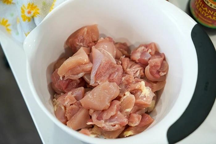 A white bowl filled with raw, chopped pieces of chicken breast, ready to become delicious meal