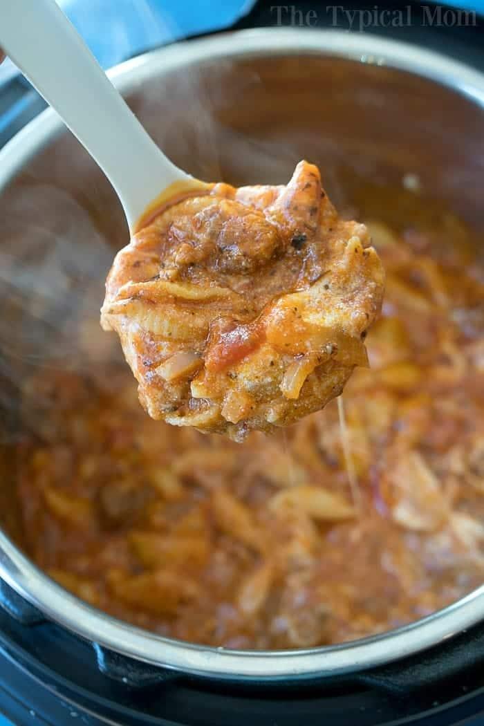 A ladle scoops cheesy pressure cooker lasagna from an Instant Pot, with steam rising.