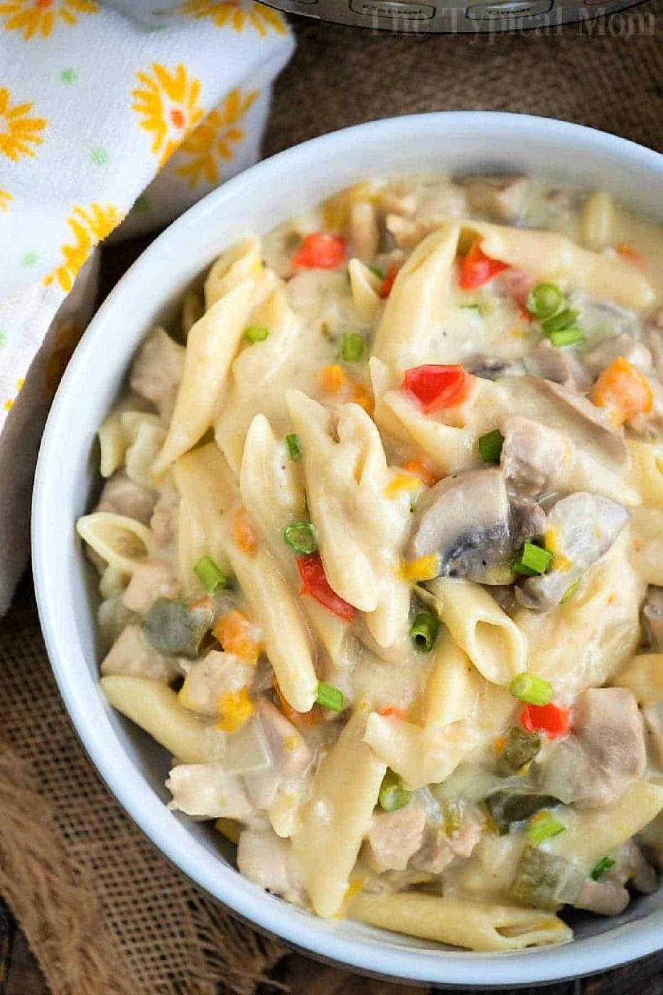 Bowl of creamy penne pasta with mushrooms, chicken, red peppers, and green onions on a rustic tablecloth—a comforting dish reminiscent of a pressure cooker lemon chicken casserole.
