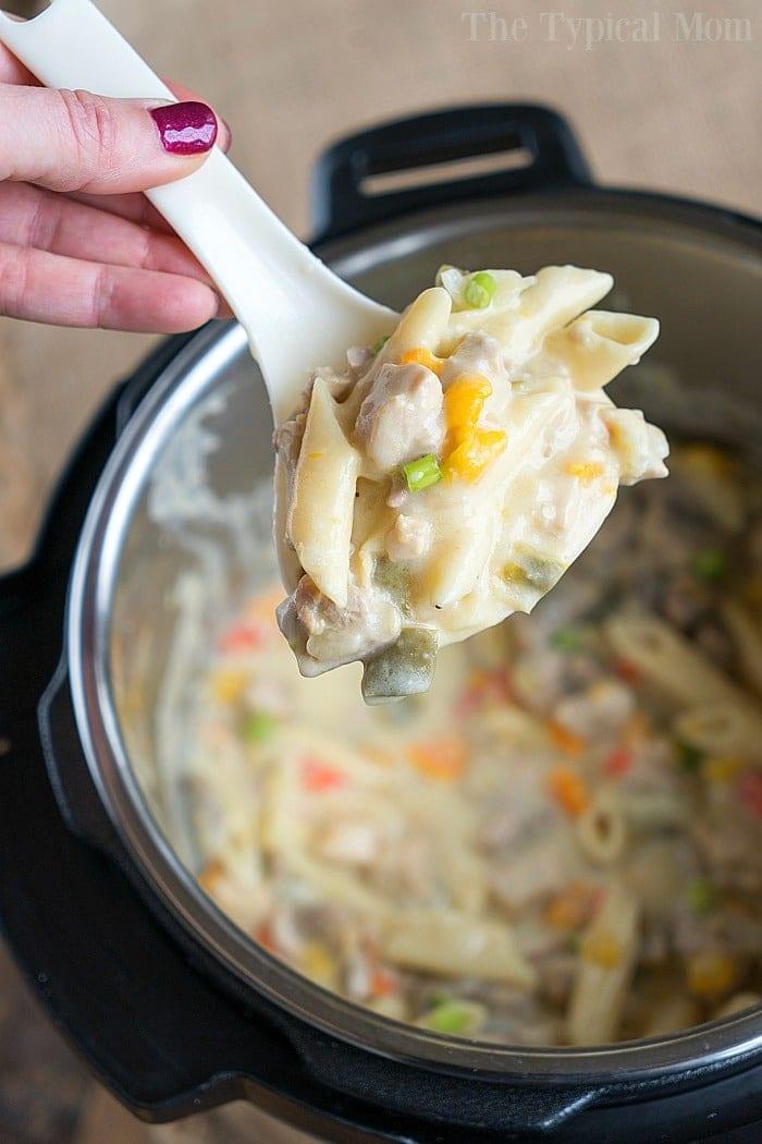 A spoonful of creamy pasta with vegetables and tender chicken, from a delicious pressure cooker lemon chicken casserole, held over a pot.