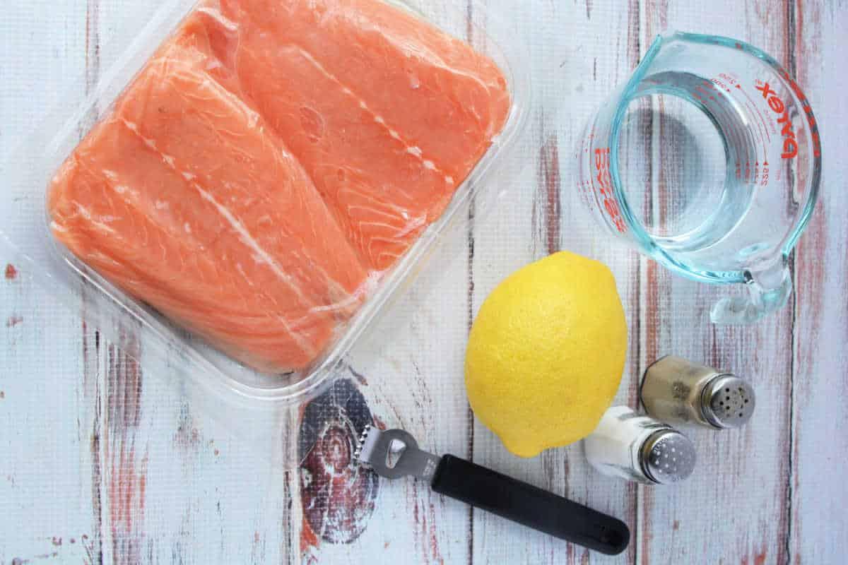 A delicious salmon recipe begins with raw fillets, a fresh lemon, and a measuring cup of water. Add salt and pepper for zest. Use a pressure cooker to infuse flavors effortlessly. Dont forget the black bottle opener nearby for your favorite refreshment.