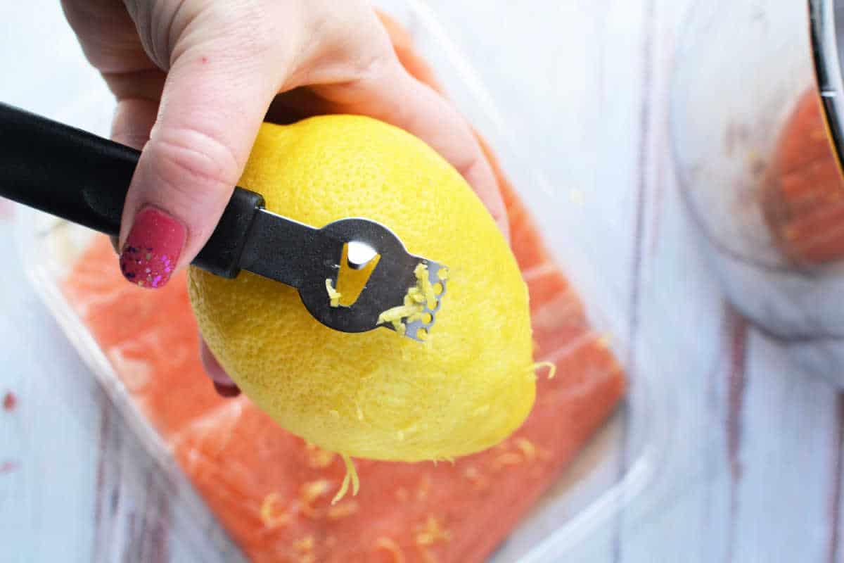 A hand expertly uses a zester to zest a lemon over a fresh container of salmon, ready to be transformed into a delightful dish. Consider using your pressure cooker for perfectly tender and flavorful results in no time.