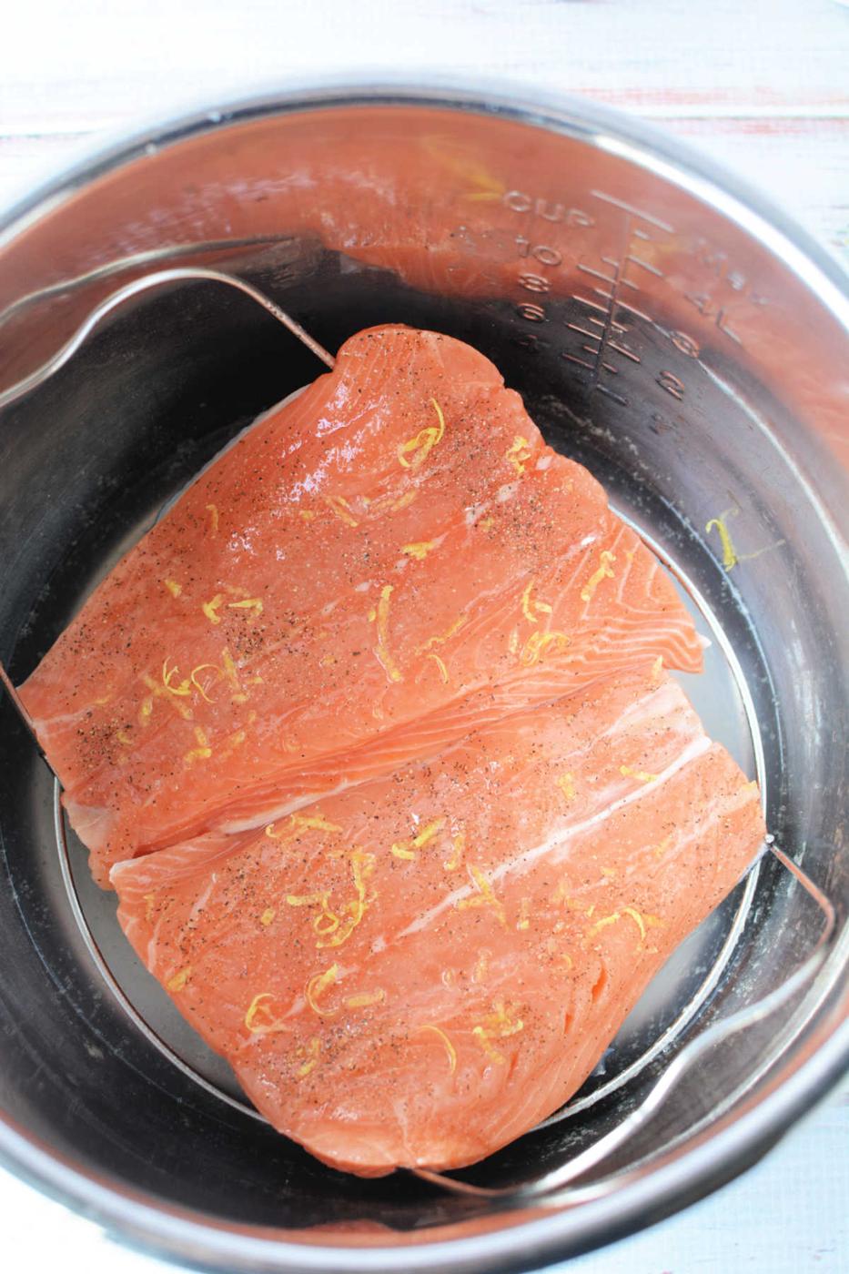 Raw salmon fillets with lemon zest and pepper, nestled in a pressure cooker for a quick and flavorful meal.