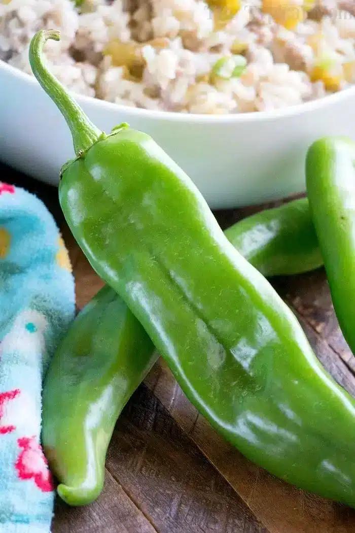 Green peppers are placed on a wooden surface next to a colorful cloth and a bowl of rice, ready to transform your meal into an instant pot sausage rice casserole.