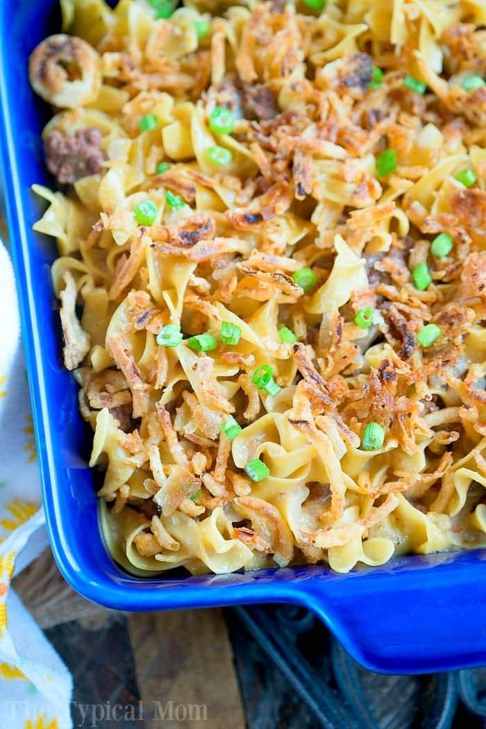 Pressure cooker stroganoff casserole with egg noodles, crispy fried onions, and chopped green onions in a blue baking dish.
