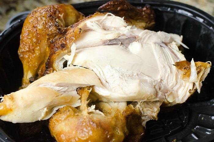 Close-up of a cooked rotisserie chicken in a black plastic container, its golden brown skin enticingly crisp. The visible white meat inside tempts you to transform it into an instant pot feel-better soup, perfect for warming up your day.