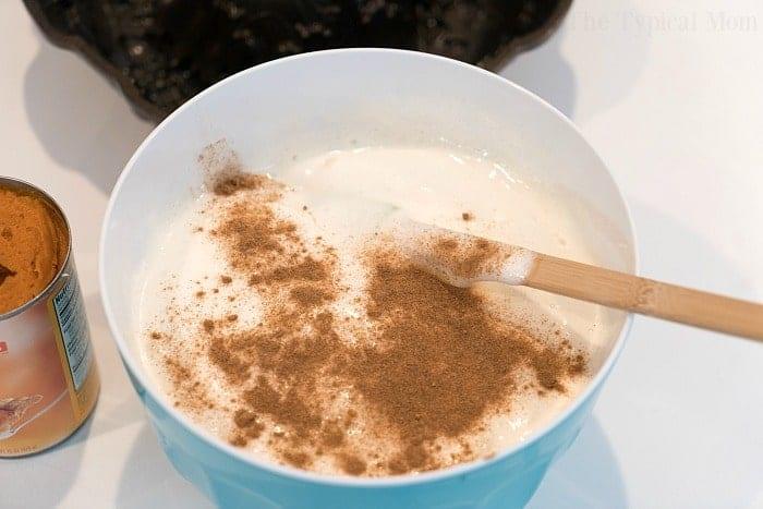A mixing bowl filled with angel food cake batter and pumpkin spice sits beside a wooden spoon, while a can of pumpkin puree waits to be transformed into a delicious pumpkin angel food cake.
