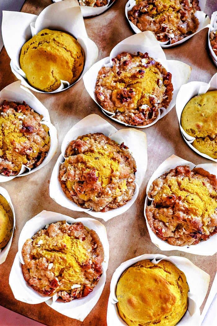 Mini pumpkin banana muffins with crumbly toppings sit in individual paper cups on a baking tray.
