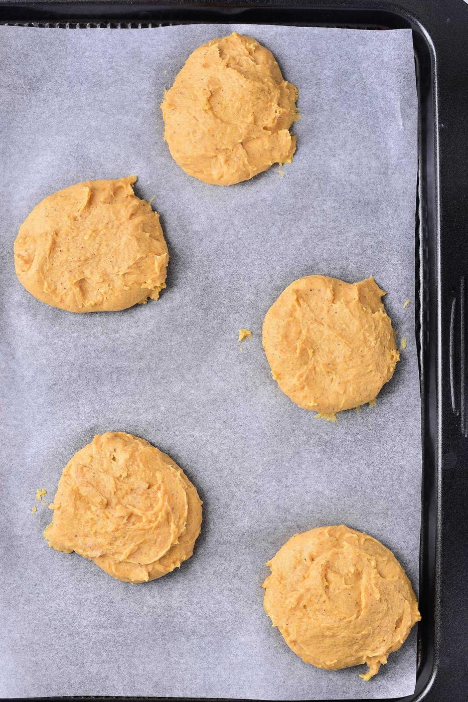 Five unbaked Pumpkin Cream Cheese Cookies, rest on a parchment-lined baking tray.