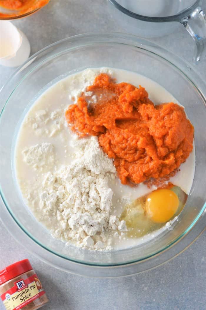 A bowl brims with pumpkin puree, Bisquick, egg, and milk mixture. Nearby, a container of pumpkin pie spice hints at the delicious transformation into fluffy pumpkin pancakes.