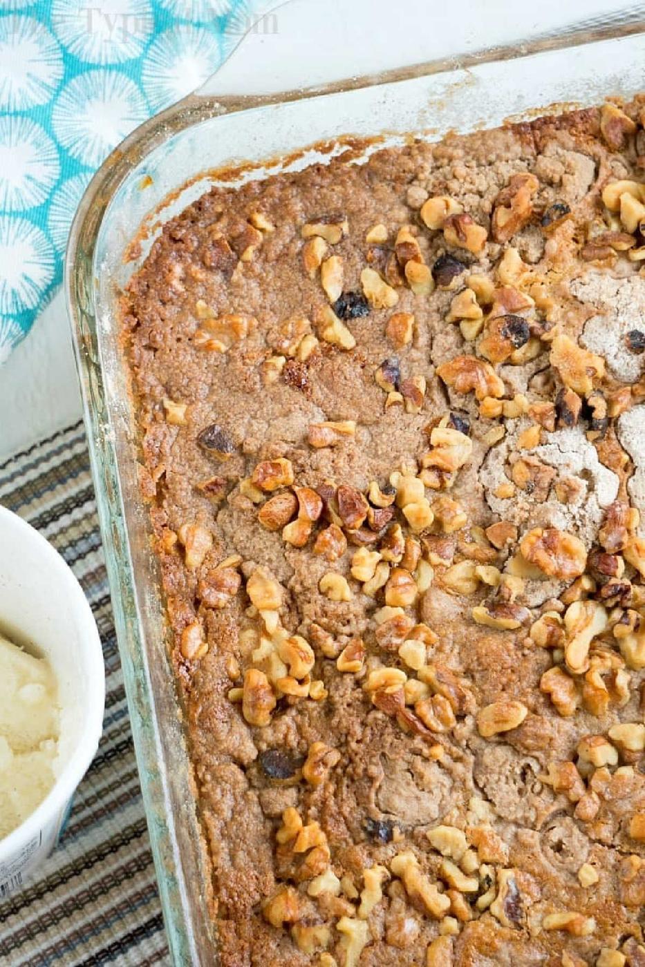 A pumpkin pie dump cake baked to perfection, topped with chopped walnuts in a glass dish, sits temptingly next to a bowl of ice cream.