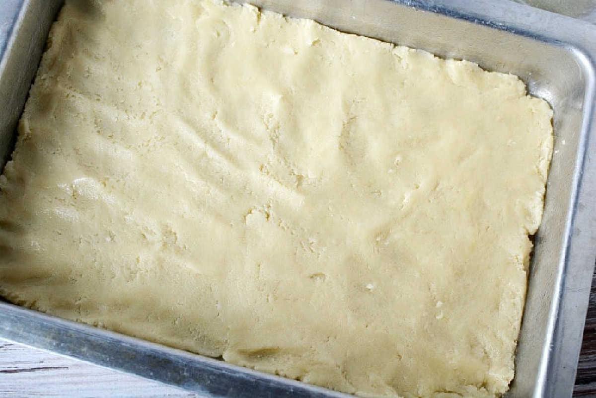 Unbaked sheet pan pumpkin pie dough evenly pressed into a rectangular metal baking pan on a light-colored surface.