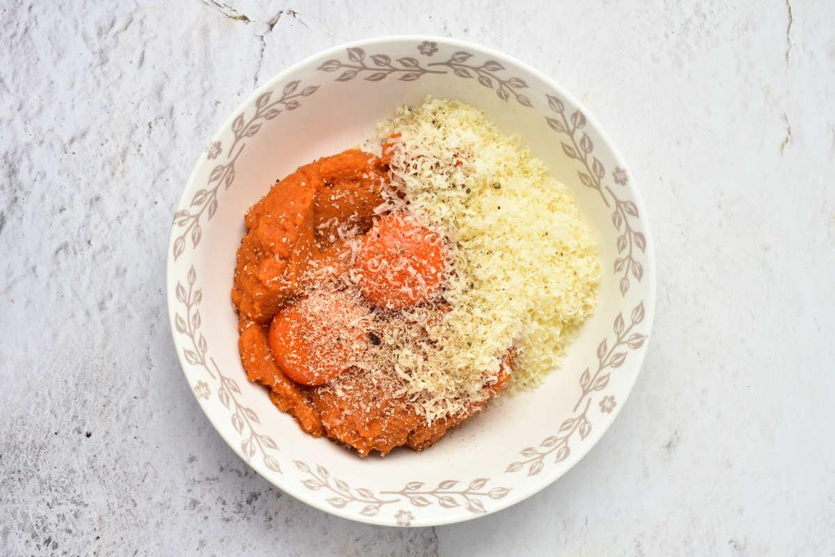 White bowl with tomato sauce and grated cheese, placed on a light marble surface—a delicious serving suggestion for Pumpkin Spaghetti or Pumpkin Noodles.