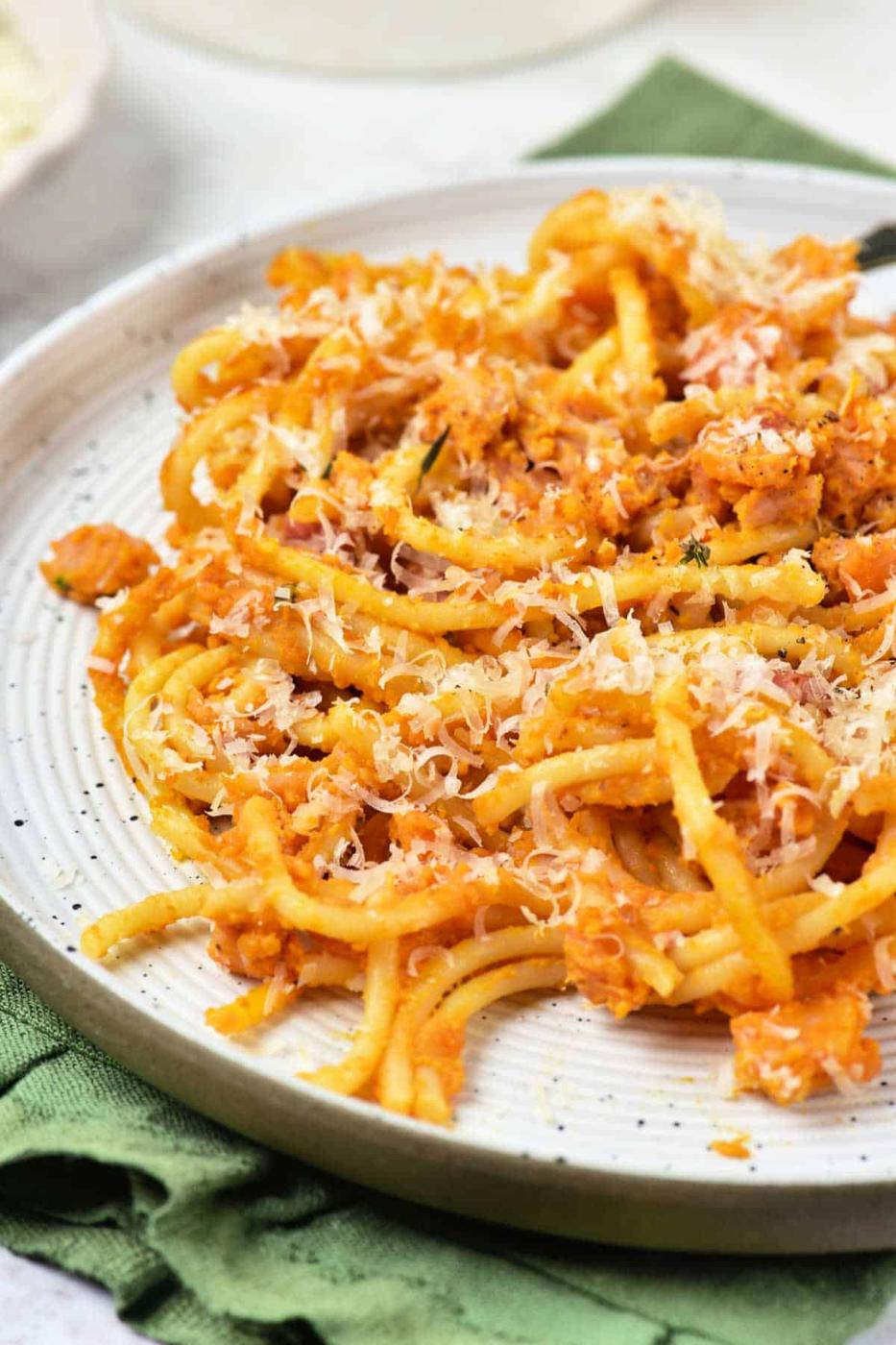A plate of delicious Pumpkin Pasta with red sauce and grated cheese, placed on a green napkin.
